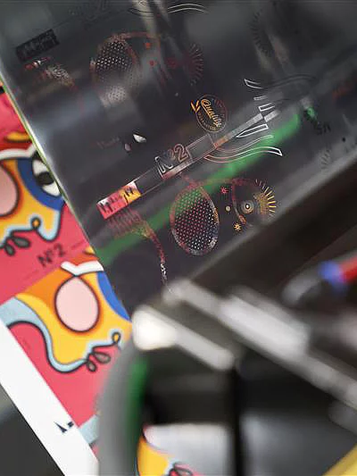 Close-up of digital embellishment process applying metallic foil to colorful printed sheets with abstract design.