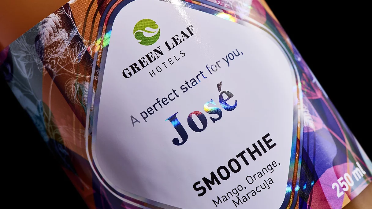 Close-up of a colorful smoothie bottle label with the text "Green Leaf Hotels," "José," and flavor details "Mango, Orange, Maracuja."