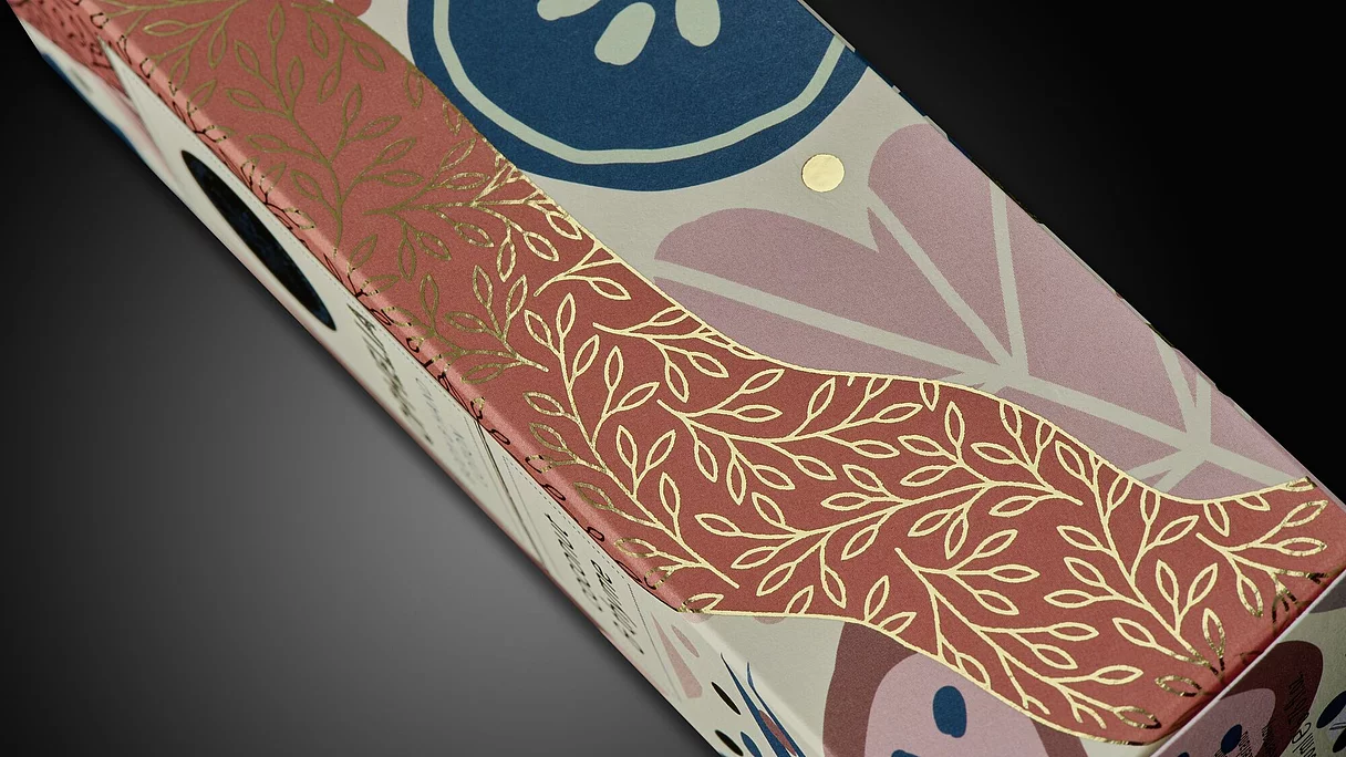 Close-up of OPHELIA cosmetic packaging with colorful floral design and gold foil embellishment, highlighting premium natural product branding.