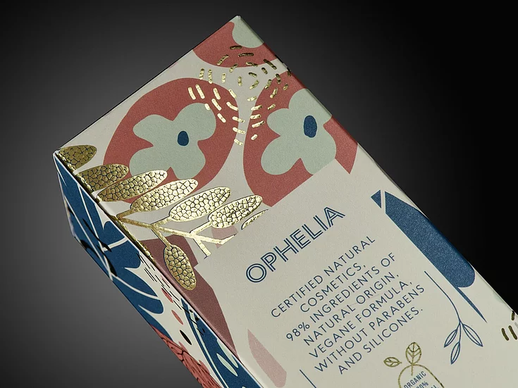 Close-up of OPHELIA cosmetic packaging with colorful floral design and gold foil embellishment, highlighting premium natural product branding.