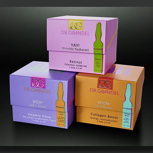 Colorful DR. GRANDEL skincare packaging boxes with metallic foil accents, featuring product names and ampoule illustrations for retinol, vitamin glow, and collagen boost.