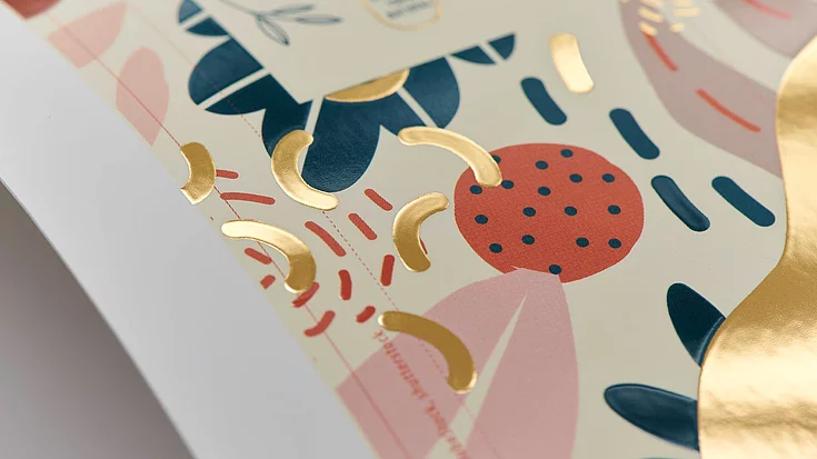 Close-up of a printed design with colorful abstract shapes and golden foil accents on a light background, showcasing detailed print finishing.