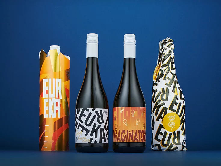 Getränkeverpackungen in verschiedenen leuchtenden Farben, die in einer Reihe auf blauem Hintergrund stehen und mit dem auffälligen Schriftzug „EUREKA“ sowie modernen Grafikdesigns versehen sind.