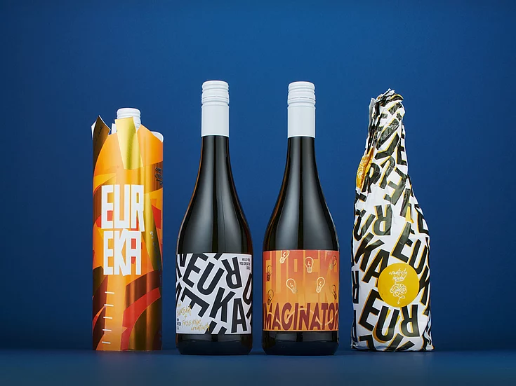 Drink packaging in various vibrant colors, standing in a row on a blue background, showcasing bold "EUREKA" text and modern graphic designs.