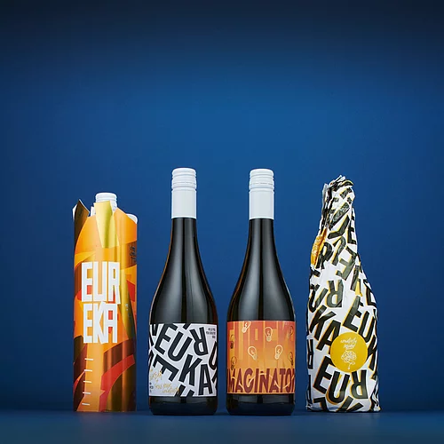 Drink packaging in various vibrant colors, standing in a row on a blue background, showcasing bold "EUREKA" text and modern graphic designs.