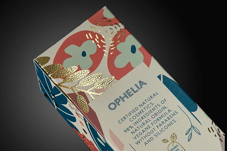 Close-up of OPHELIA cosmetic packaging with colorful floral design and gold foil embellishment.