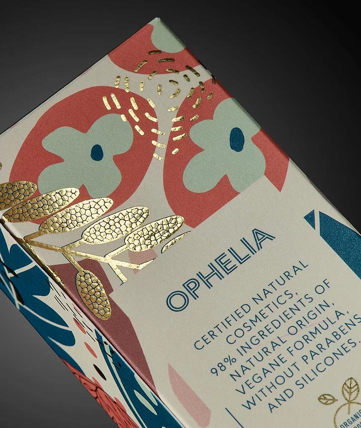 Close-up of OPHELIA cosmetic packaging with colorful floral design and gold foil embellishment.