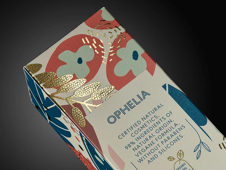Close-up of OPHELIA cosmetic packaging with colorful floral design and gold foil embellishment.
