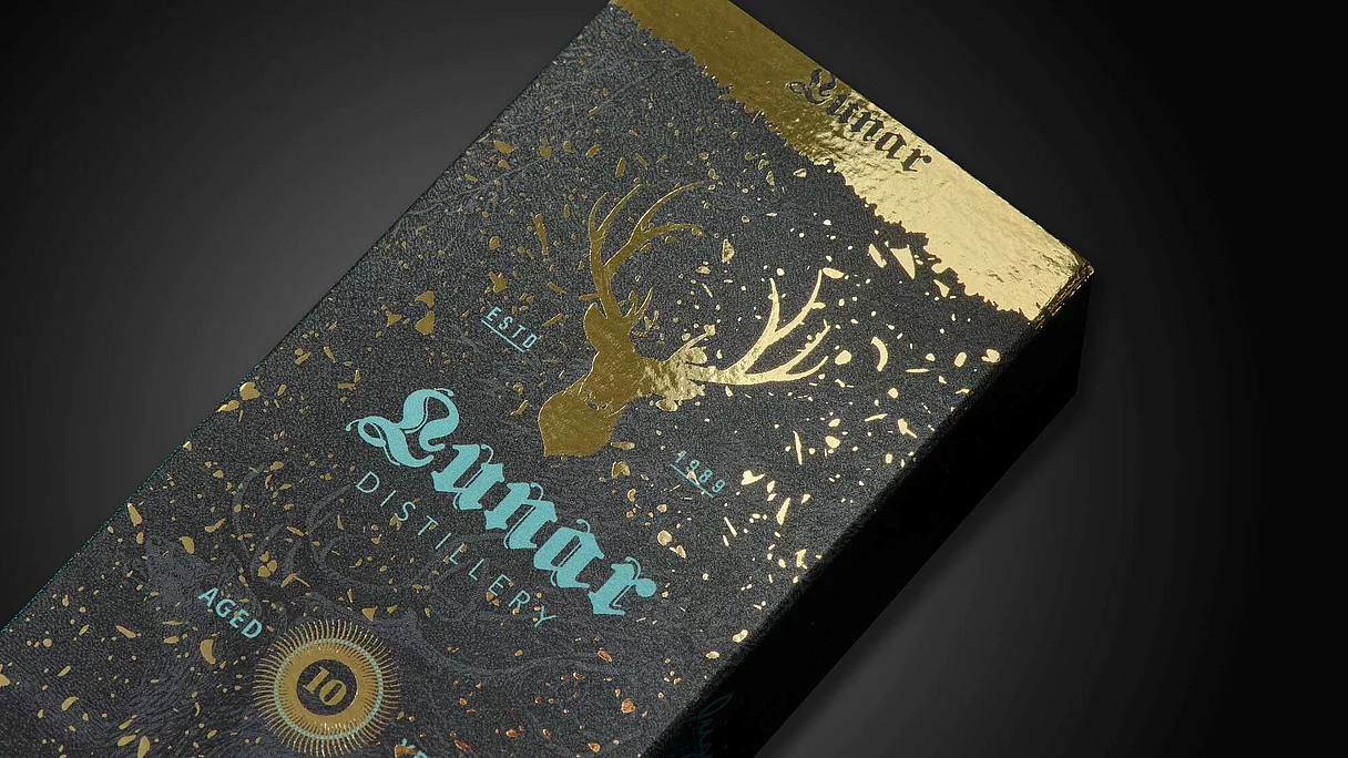 Black and gold packaging box with a gold foil deer head and decorative splashes, labeled "Lunnar Distillery" aged 10 years.