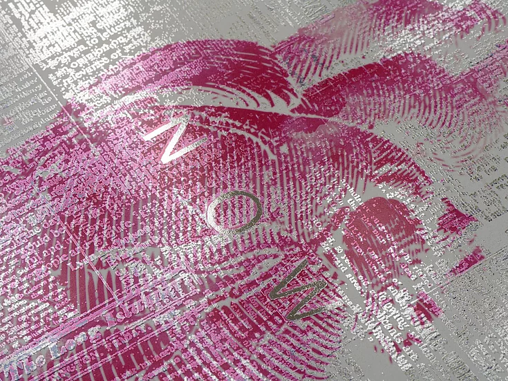 Close-up of a textured print with pink brush strokes and silver text forming the word ‘NOW’ on a metallic background.