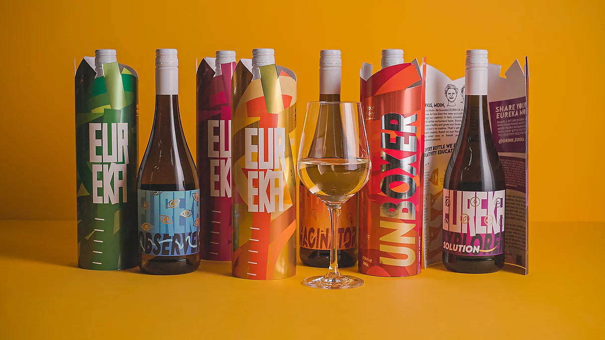 Six colorful wine bottles in decorative sleeves with bold text and designs, arranged in a row on a yellow background, with a glass of white wine in front.