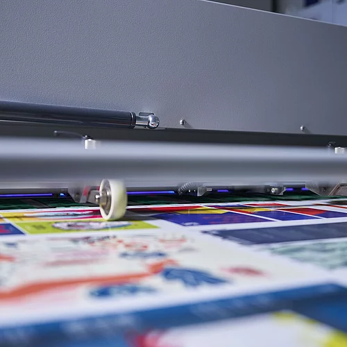 Close-up of a printing machine applying colorful graphics on a flat surface, focusing on small rollers guiding the print material.
