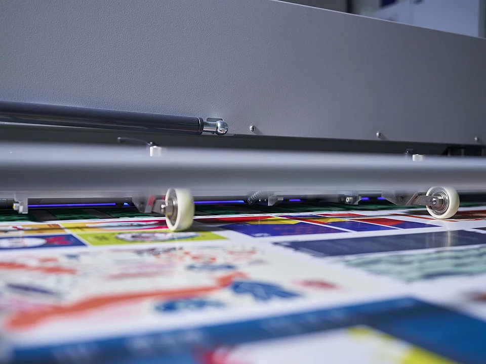 Close-up of a printing machine applying colorful graphics on a flat surface, focusing on small rollers guiding the print material.