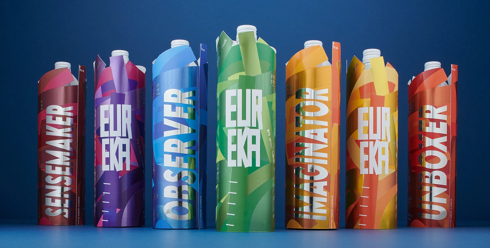 Getränkeverpackungen in verschiedenen leuchtenden Farben, die in einer Reihe auf blauem Hintergrund stehen und mit dem auffälligen Schriftzug „EUREKA“ sowie modernen Grafikdesigns versehen sind.