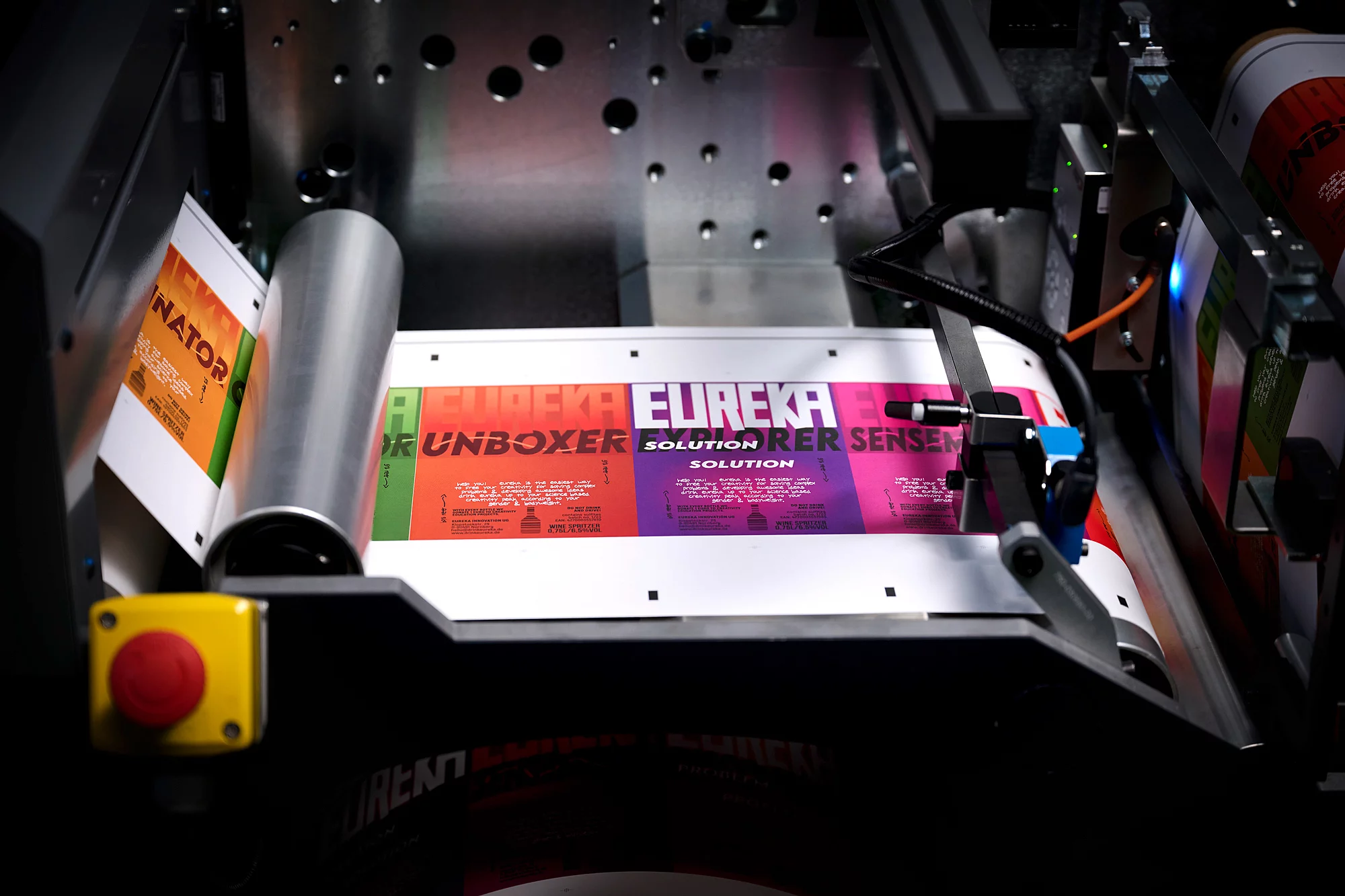 This is a close-up of a printing machine producing colorful labels with the word "EUREKA."