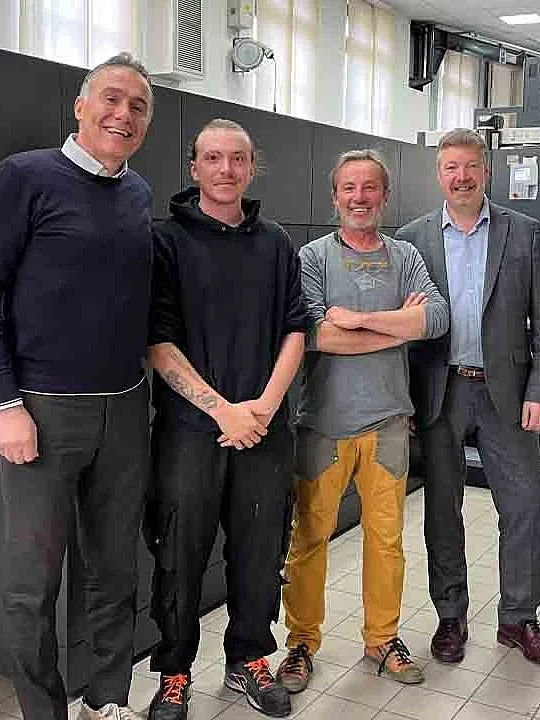 Four men smiling side by side in a modern production hall