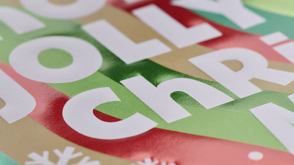 Close-up image showing vibrant holiday graphics with metallic red and green foil elements on packaging, including embossed white snowflakes and text.