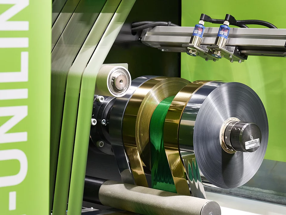 Digital Embellishment Solution with green panels, multiple rollers, two screens, and roll-fed colorful label material.