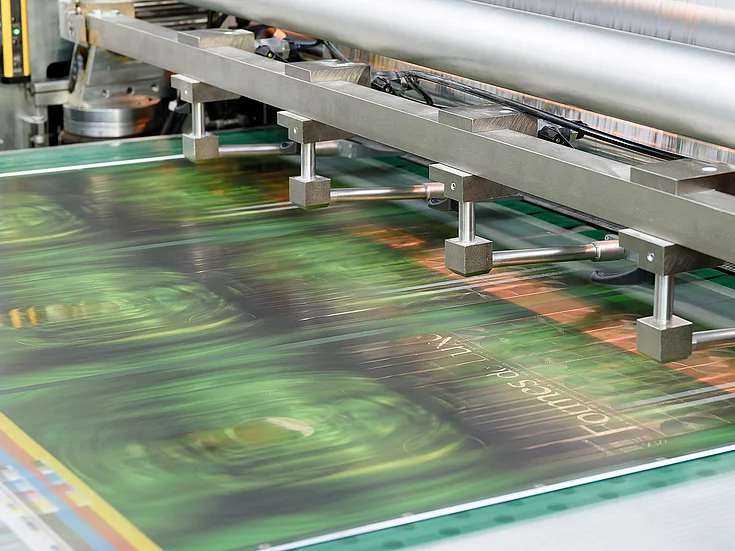 Close-up of printing machine producing glossy sheet with green and gold patterns and the text “Formes de Luxe.”