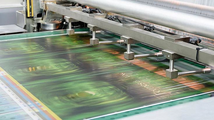 Close-up of a printing press producing a glossy sheet with green and gold geometric patterns and the text ‘Formes de Luxe’.