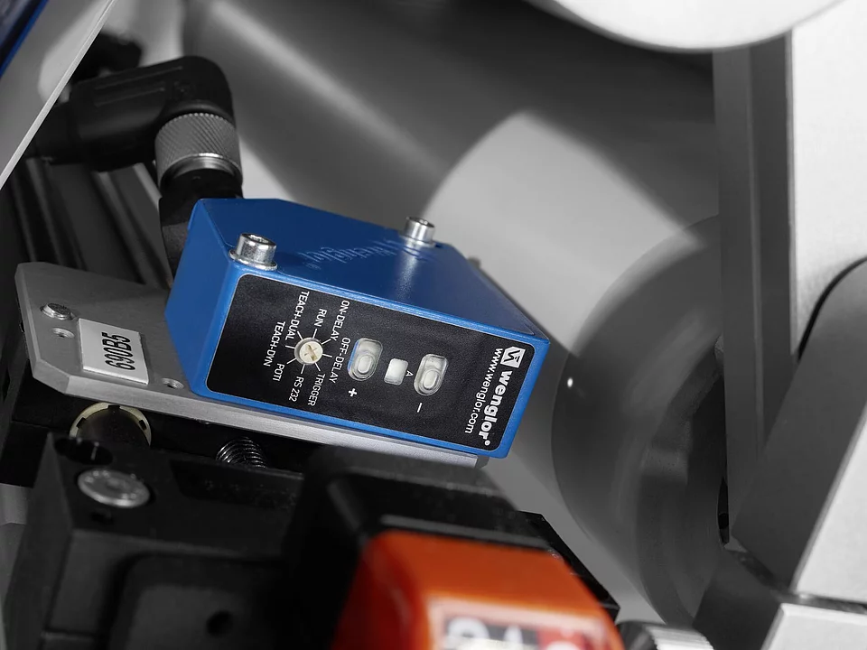 Close-up of a blue Wenglor sensor device attached to machinery with a spinning roller in the background.