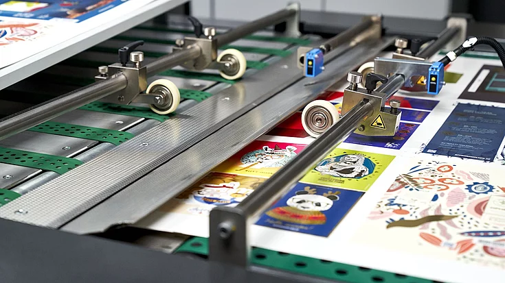 Close-up of a printing machine producing colorful sheets featuring various cartoon and artistic designs