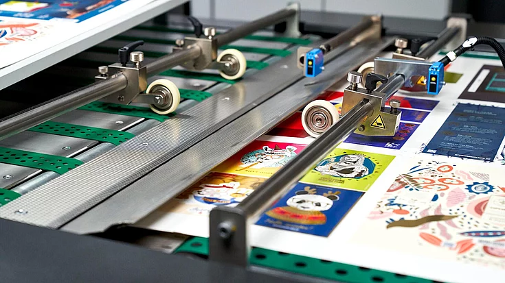 Close-up of a printing machine producing colorful sheets featuring various cartoon and artistic designs