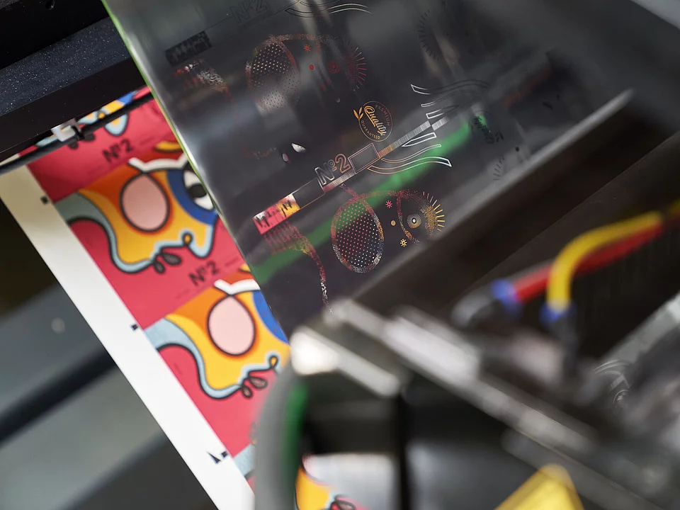Close-up of printing process with colorful abstract labels and transparent film featuring metallic details.