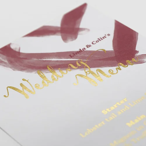 Wedding menu card with gold foil lettering and burgundy brushstrokes.