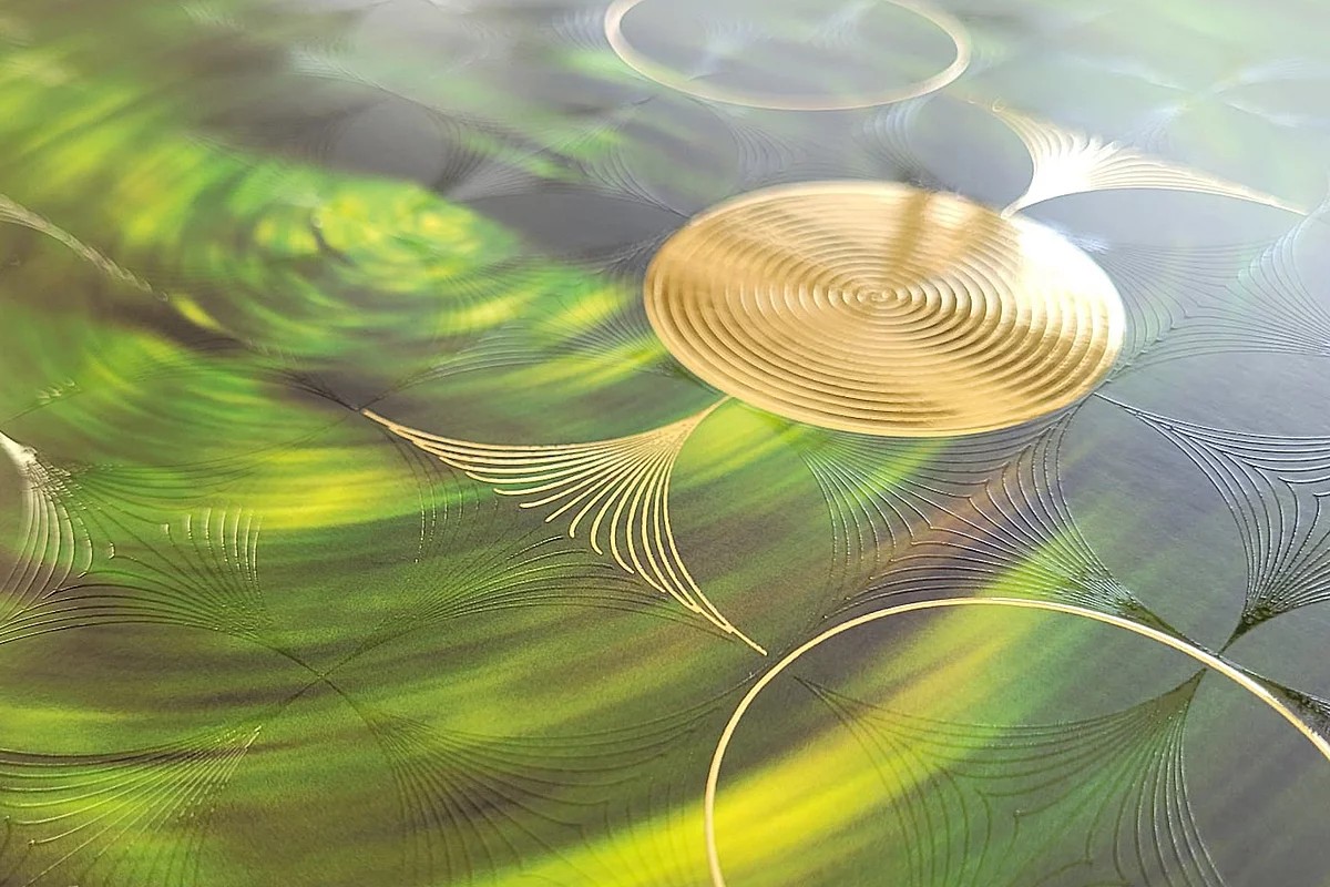 Close-up of a green surface with intricate gold embossed circular and geometric patterns reflecting light.