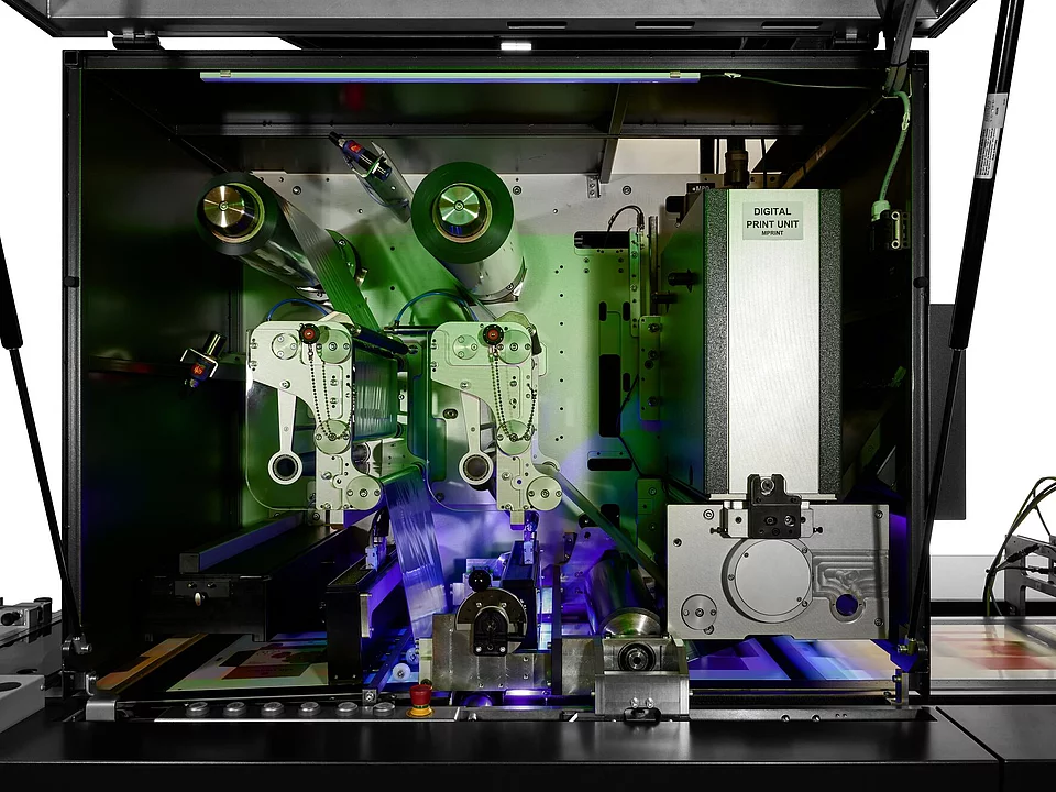 Inside view of a digital print unit machine with rollers and conveyor system for labels or packaging.